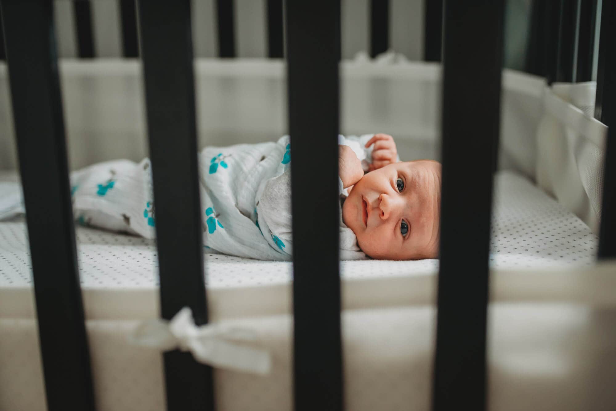 baby looks through crib bars at lifestyle newborn session