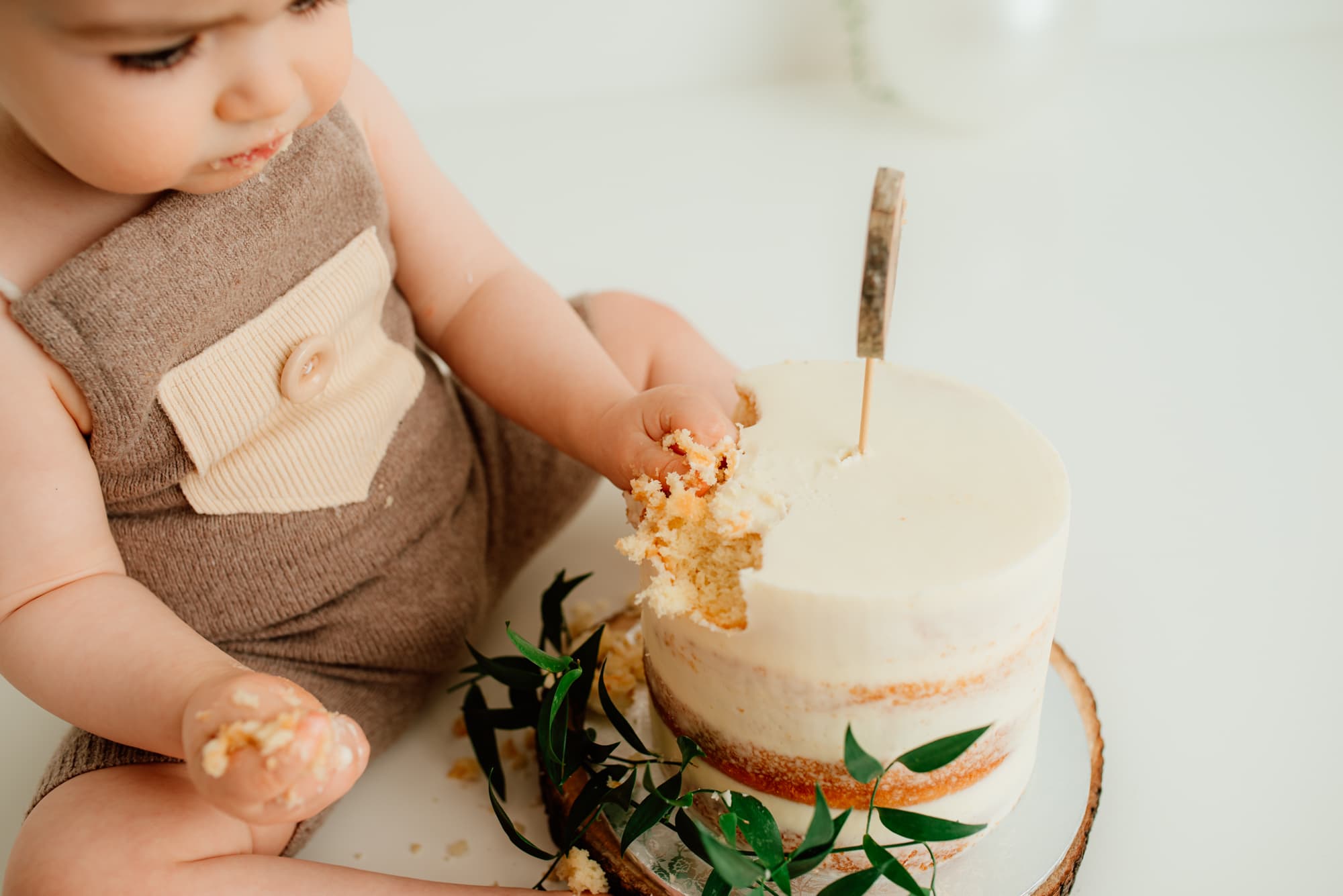Close-up of little baby fingers digging into a semi-naked cake during his cake smash session.