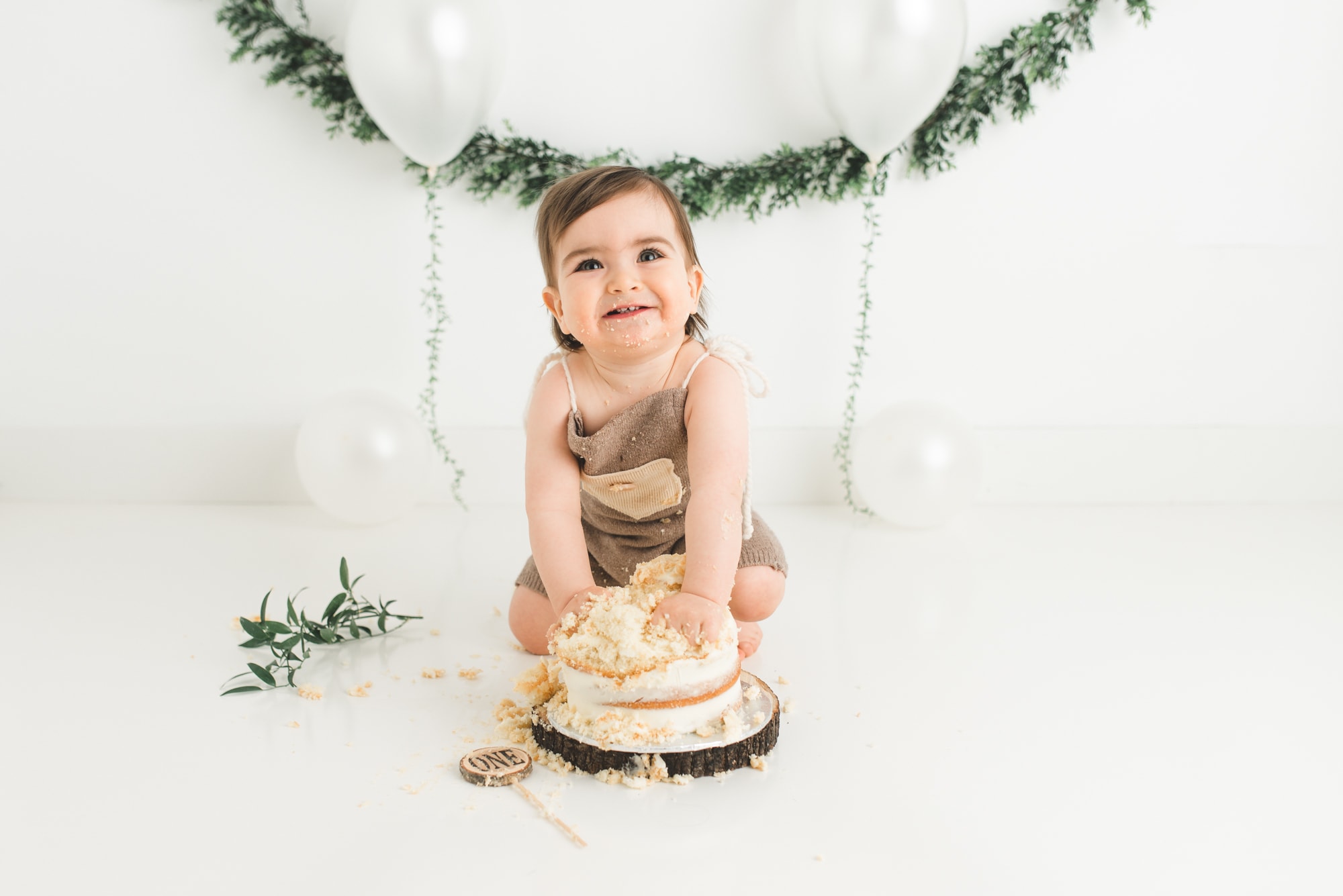 Toddler boy smashing his cake in a white studio with natural elements