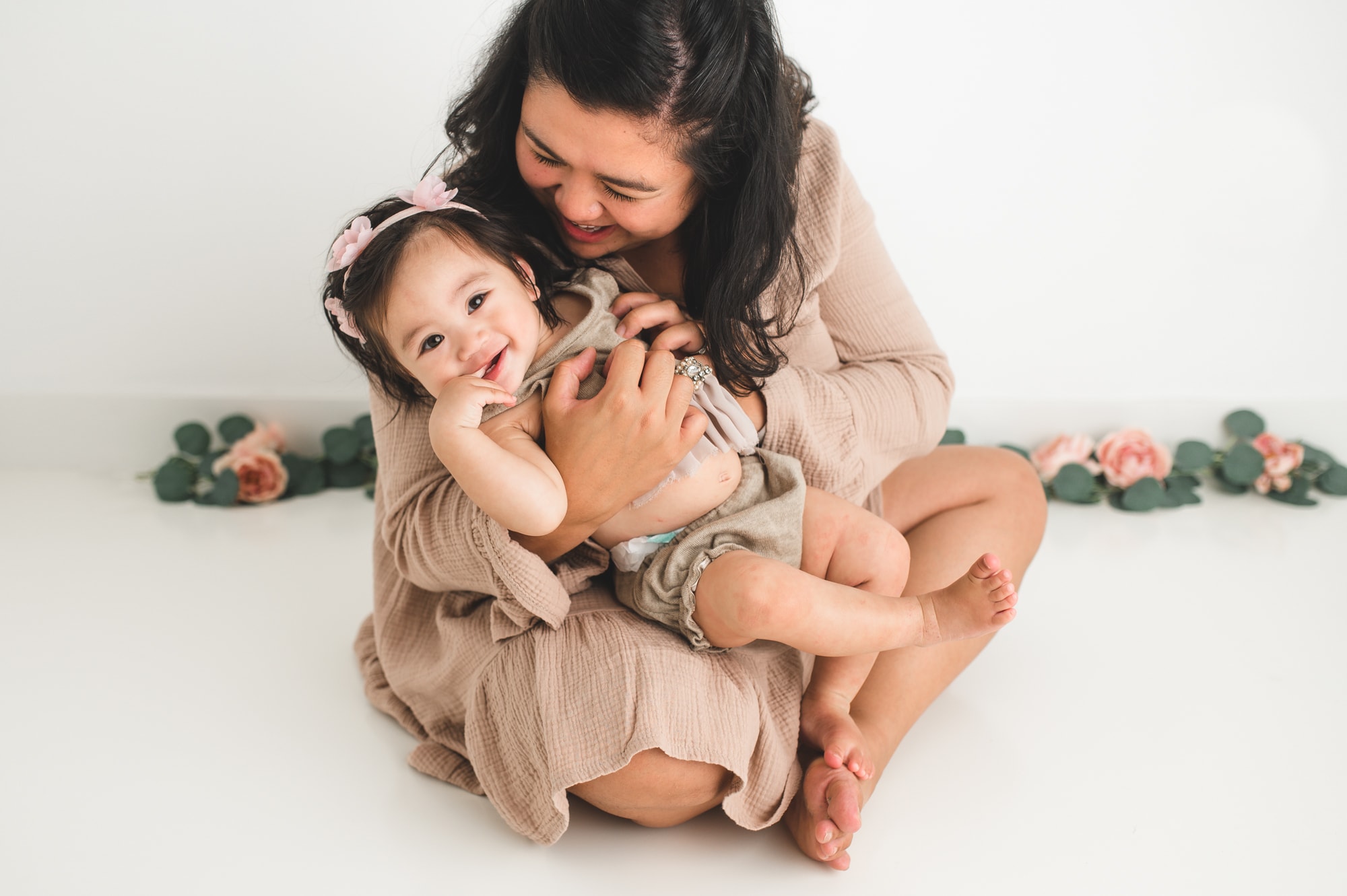 Mom and daughter in neutral dresses cuddle and laugh in a Coquitlam photo studio.