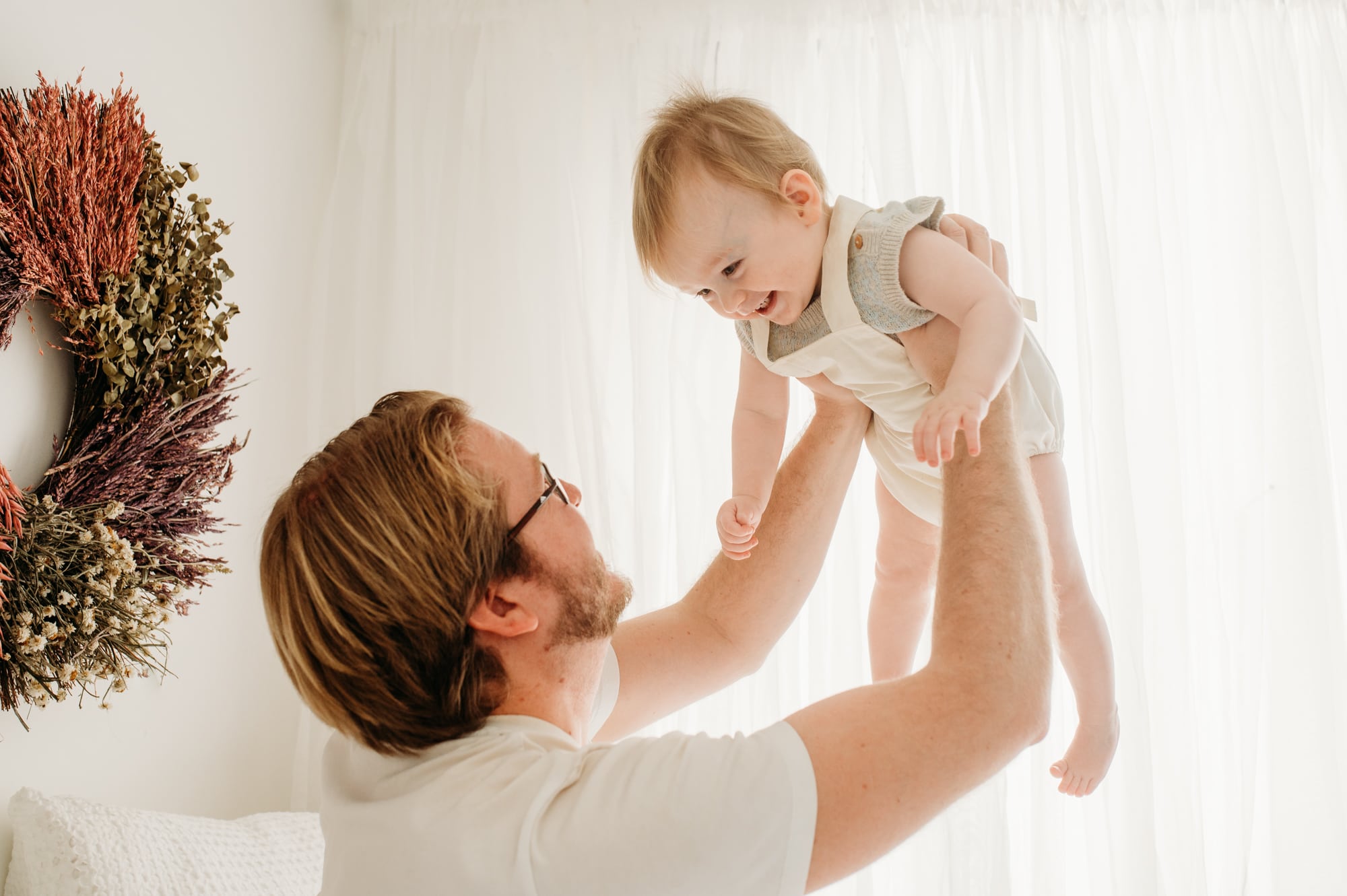 Dad lifts his baby boy into the air inside a Vancouver studio with white curtains.