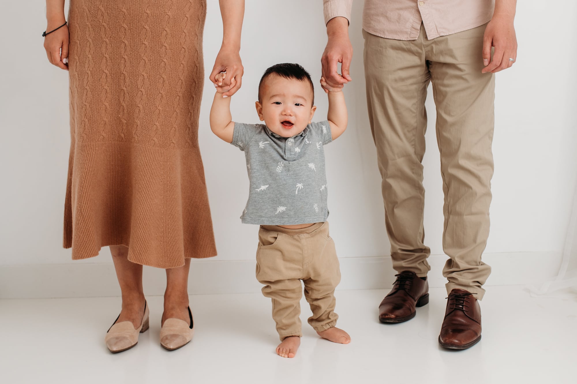 Asian boy holds hands with his parents in their family photo in a Vancouver studio.