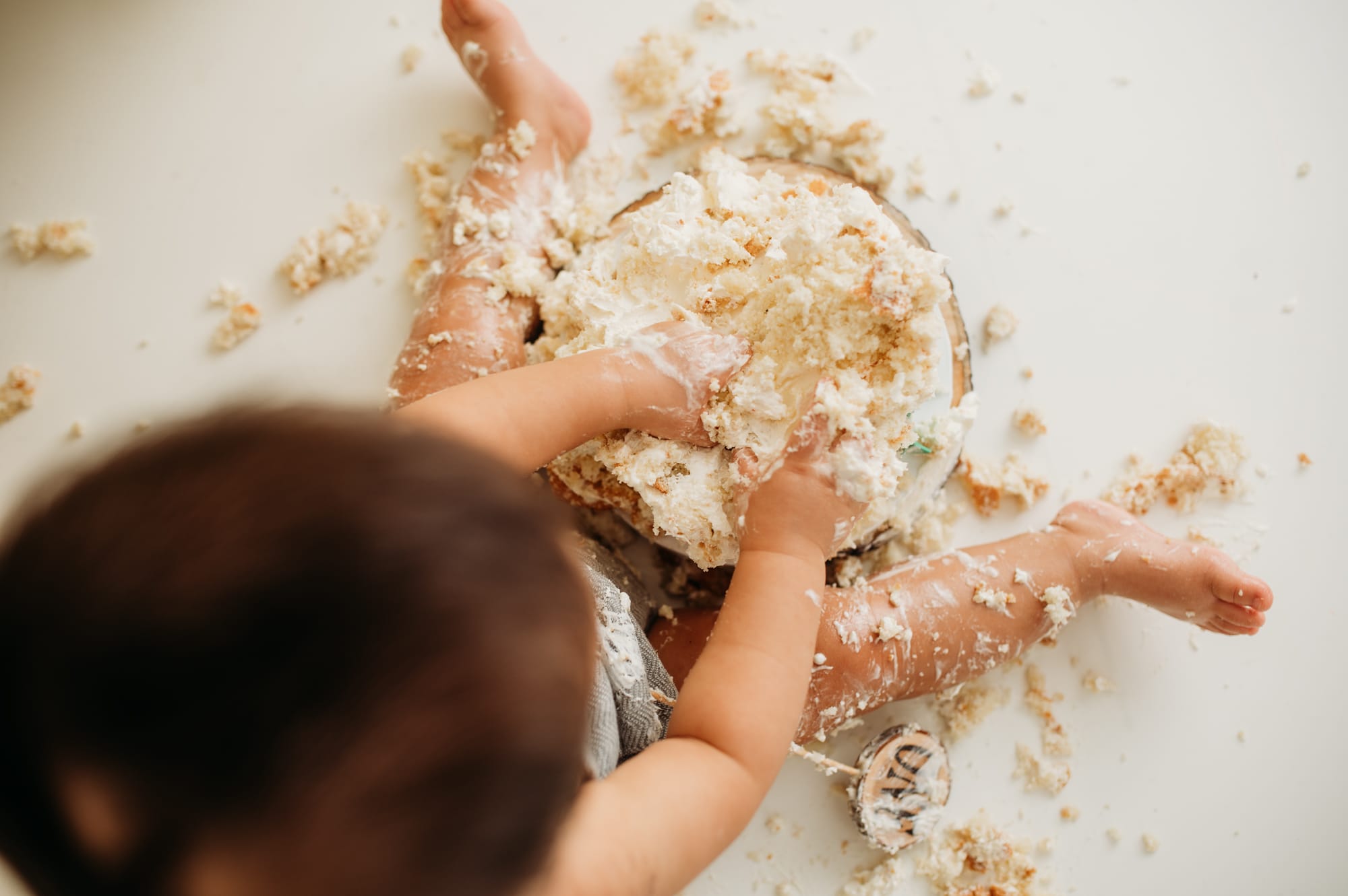 Cake smashing! Child digs their fingers through a destroyed cake during cake smash session.