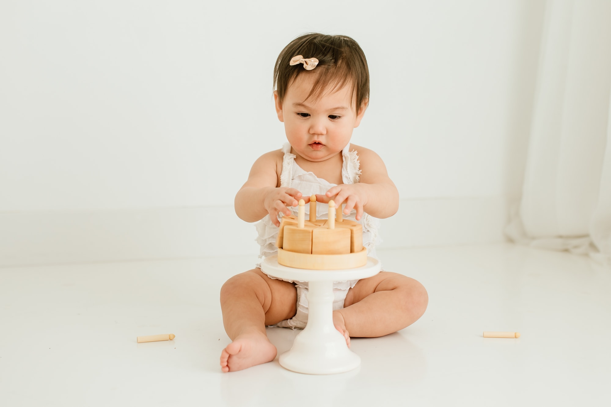 One year old girl plays with wooden cake toy to celebrate her first birthday with a portrait session.