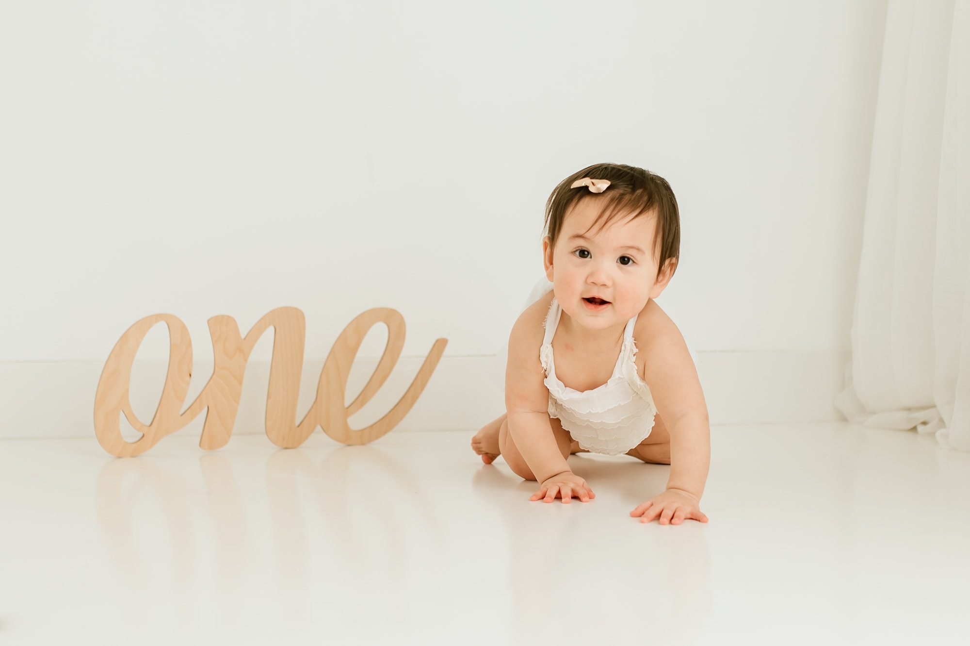 Baby girl crawls next to a wooden sign saying one in a simple and modern first birthday cake smash session.
