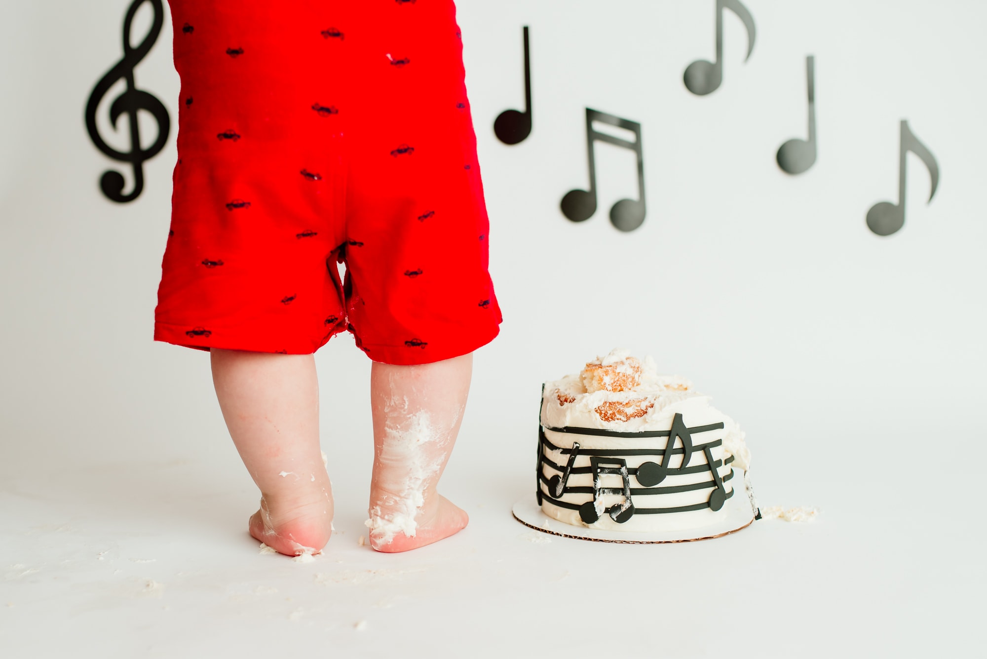 Just the chubby legs of a boy in bright red overalls during his music themed cake smash.
