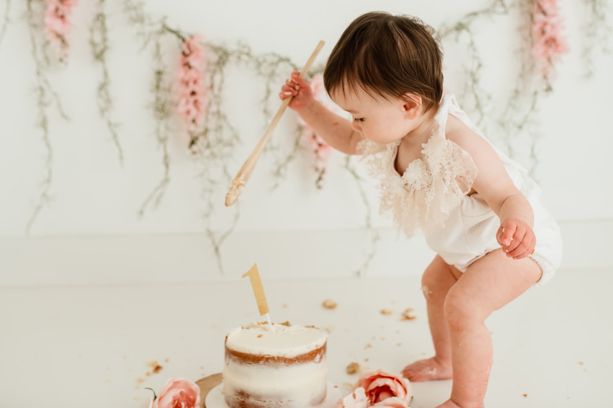 Toddler girl smashing her cake with a wooden spoon.
