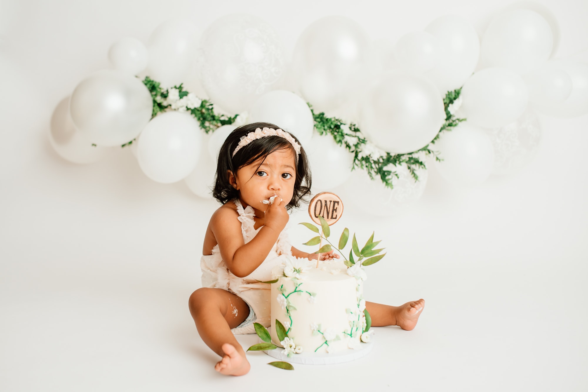 East-Indian baby girl with her fingers in her mouth, eating cake during her cake smash session.