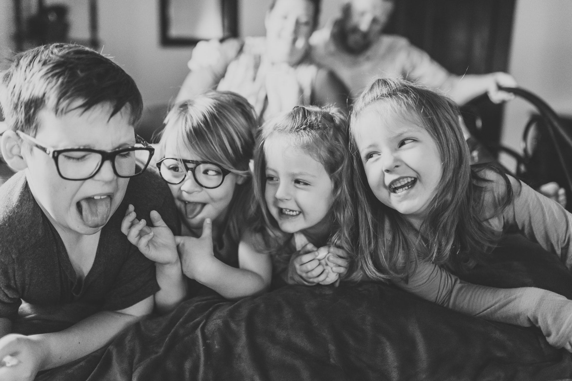 4 siblings lying side by side on bed pulling faces at each other