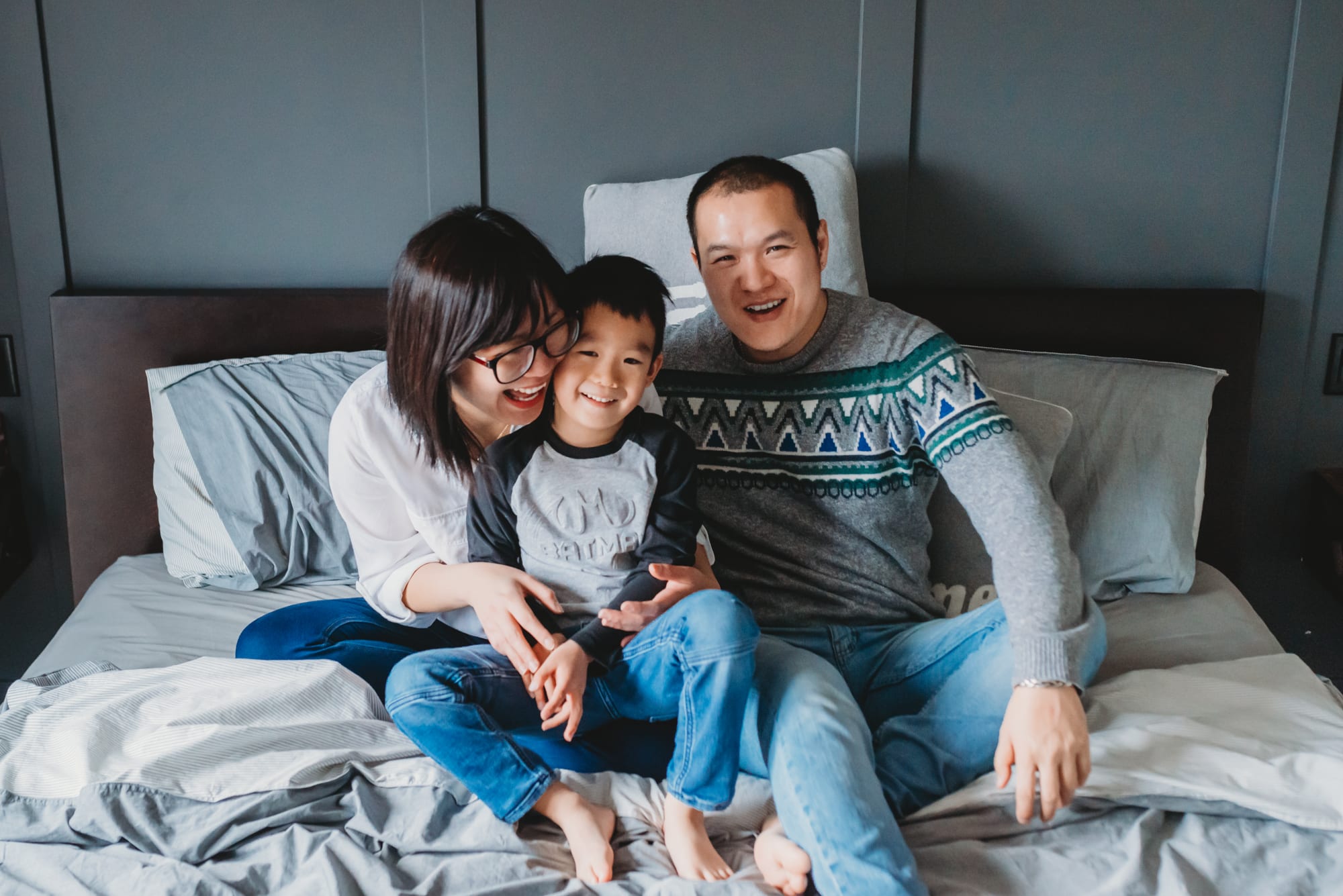 Fun family photo of Asian parents and their son laughing on the bed in the master bedroom.