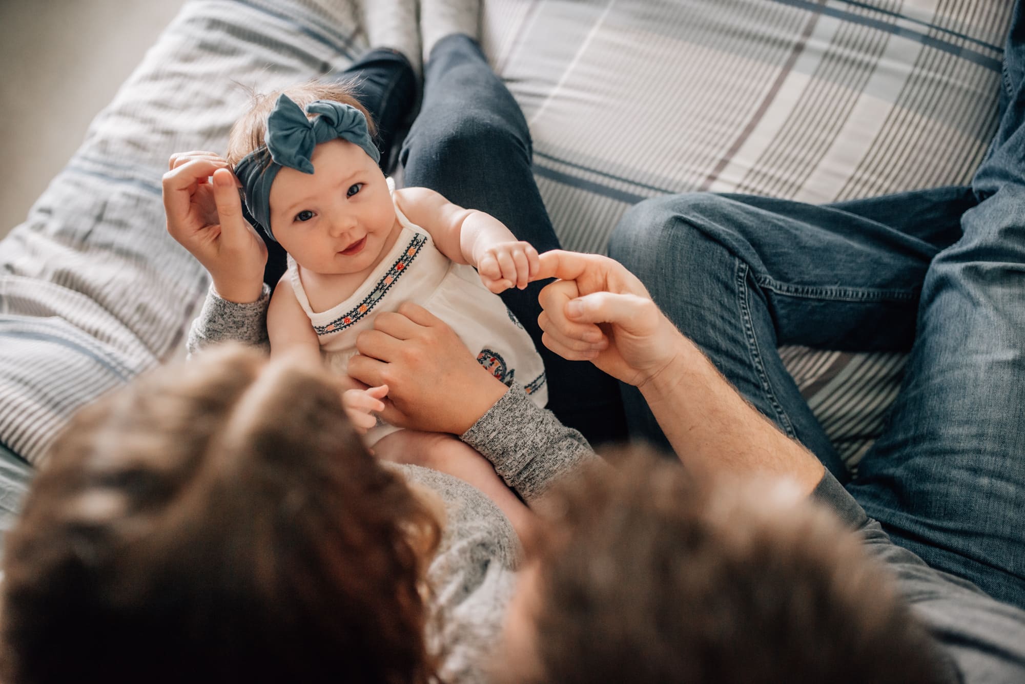 Couple look down at their baby girl with her hand curled around dad's finger in tender Vancouver family photo session inside their home.