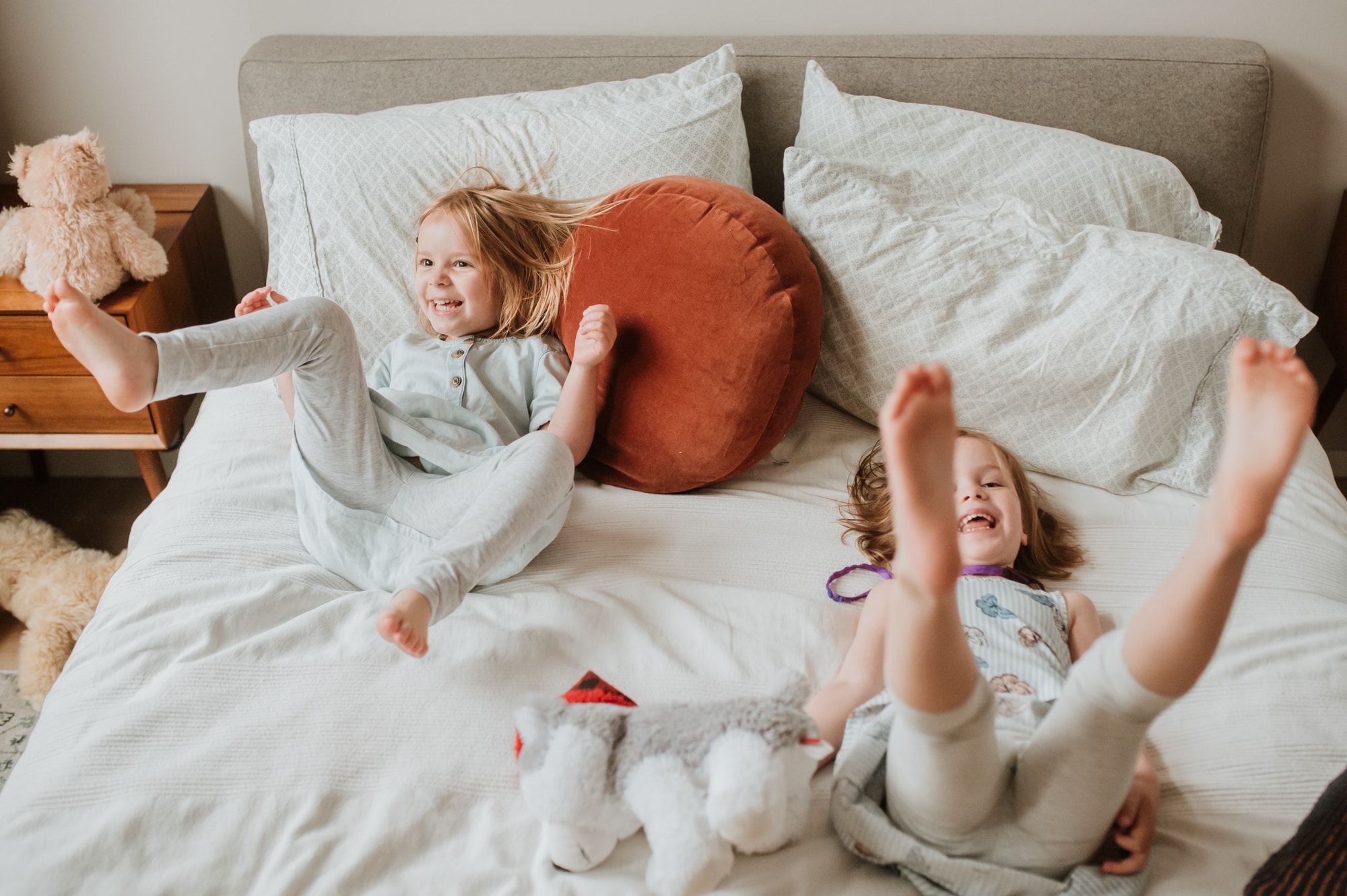 Two girls jumping wildly on their parents' bed in fun Vancouver family photos.