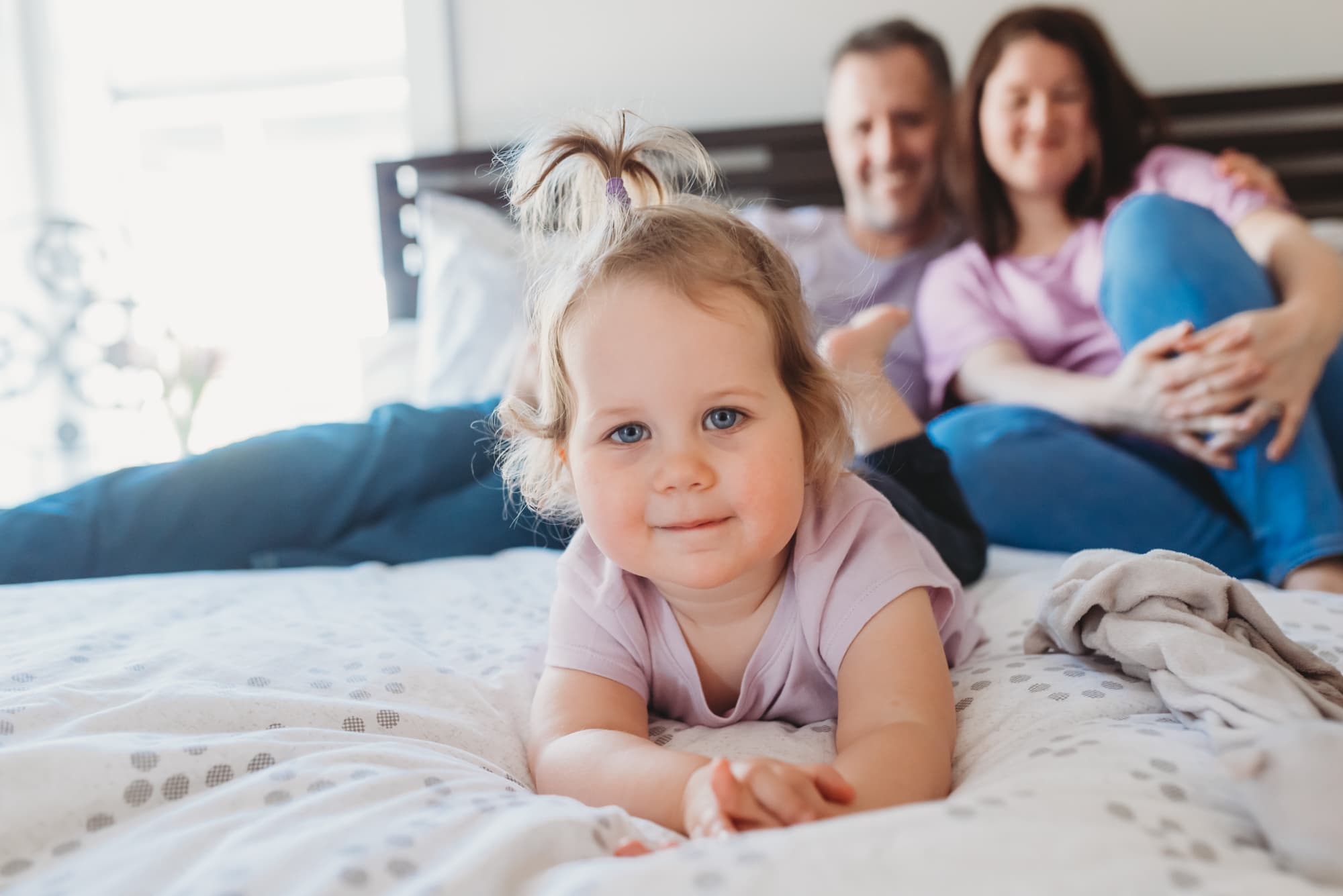 girl with blue eyes lying on bed with parents during Port Coquitlam family photo session