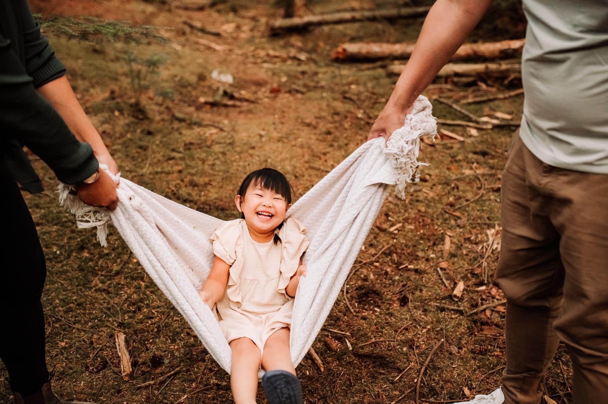 Asian girl laughs as she is being swung in a blanket in a Point Grey family photography session.