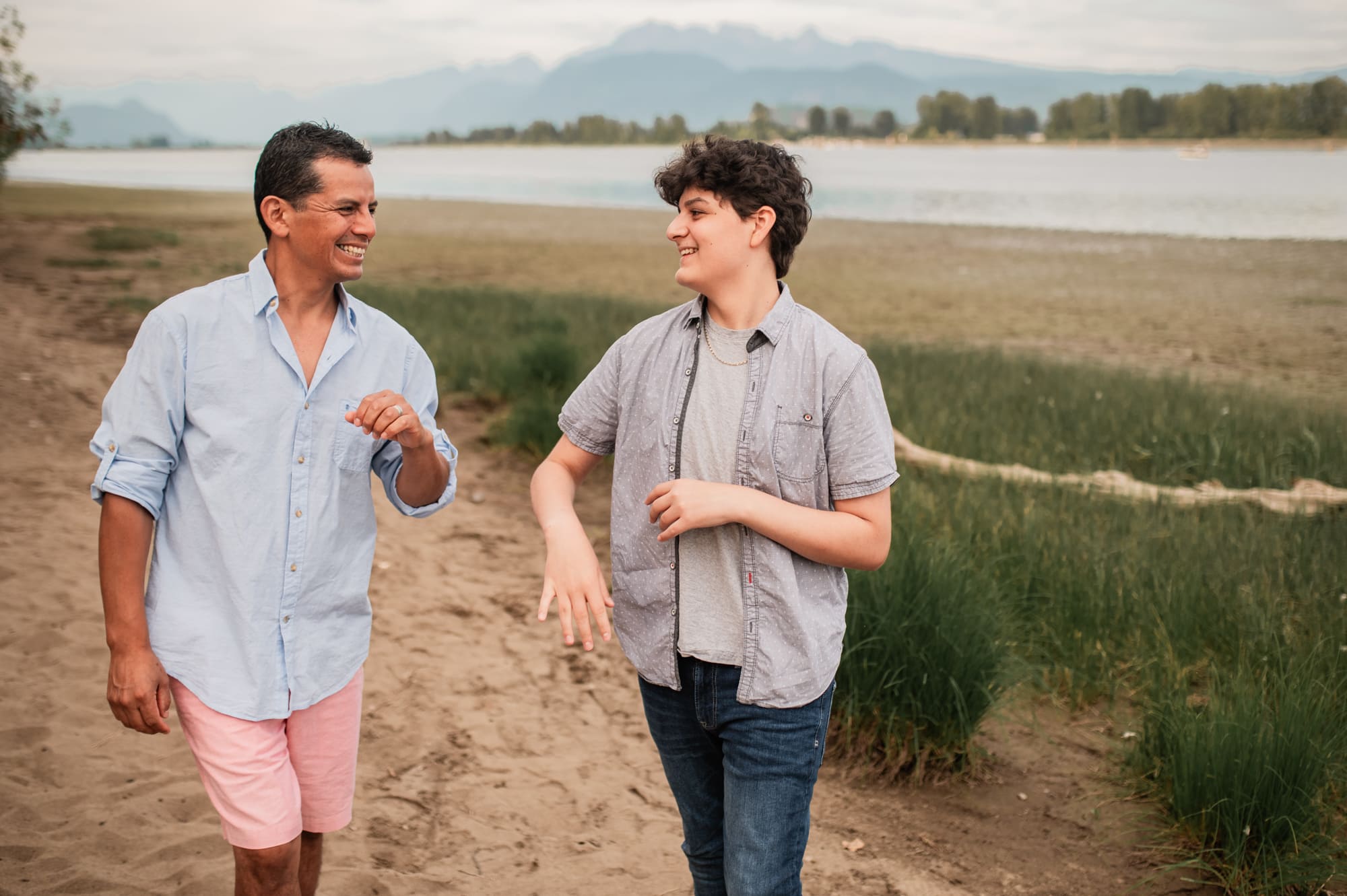 Latino dad and son laugh together with Pitt River and Golden Ears Mountains in the background.