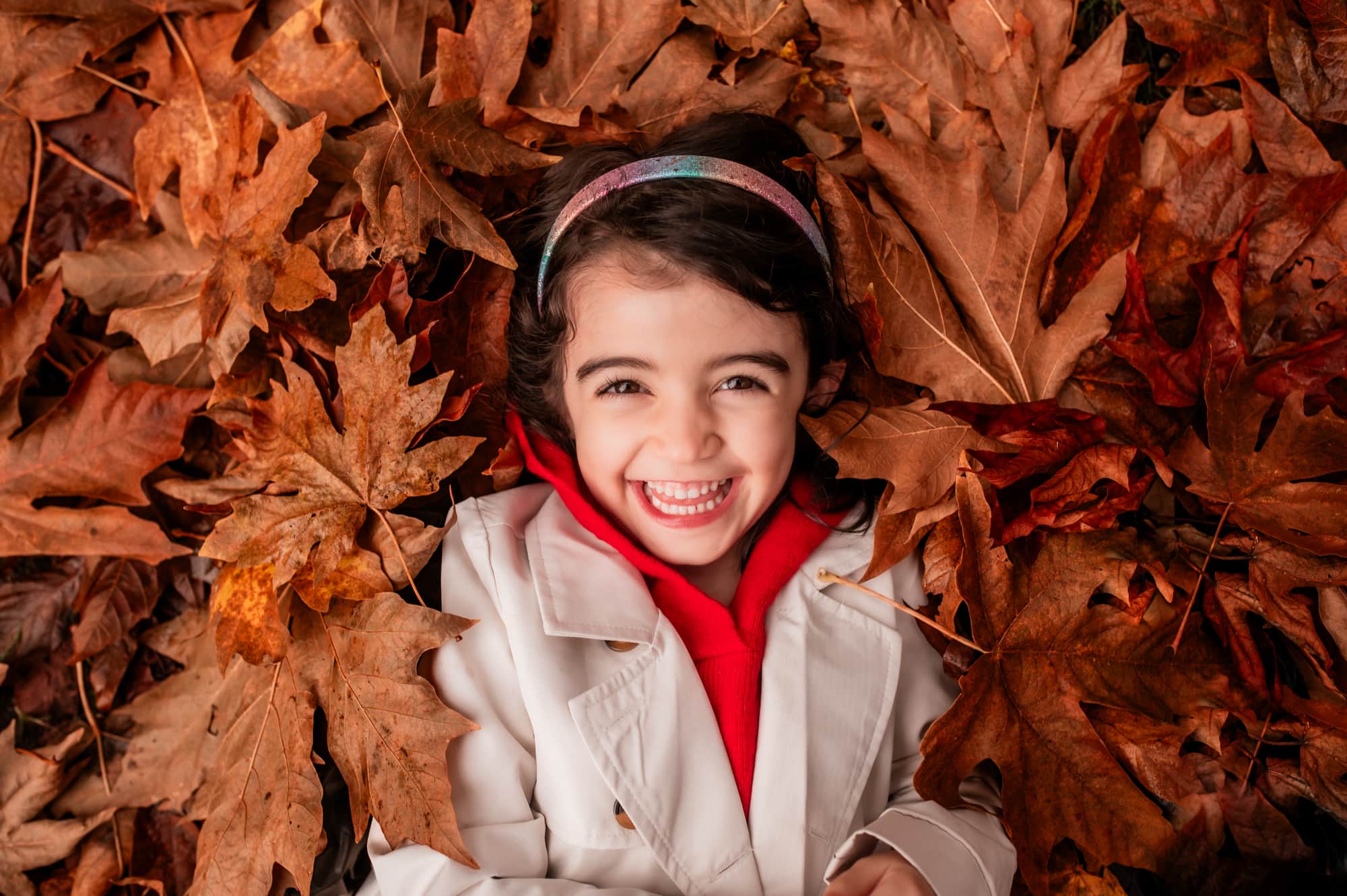 Girl lies in autumn leaves and laughs at the family photographer.