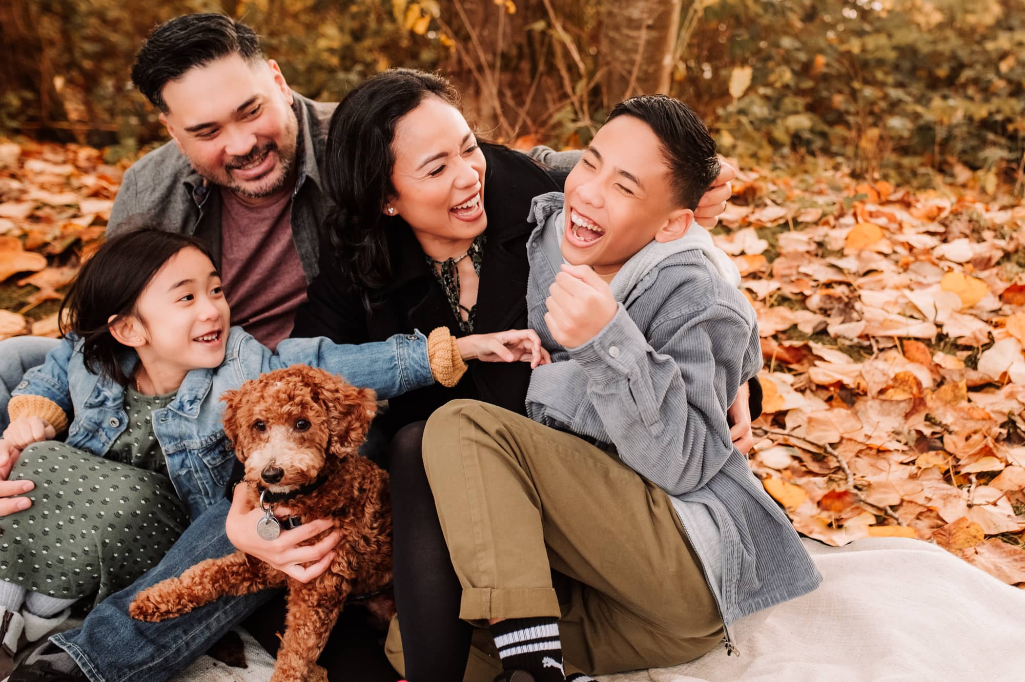 Teenage boy laughs as he is being tickled by his Pitt Meadows family during a fall family photo shoot.
