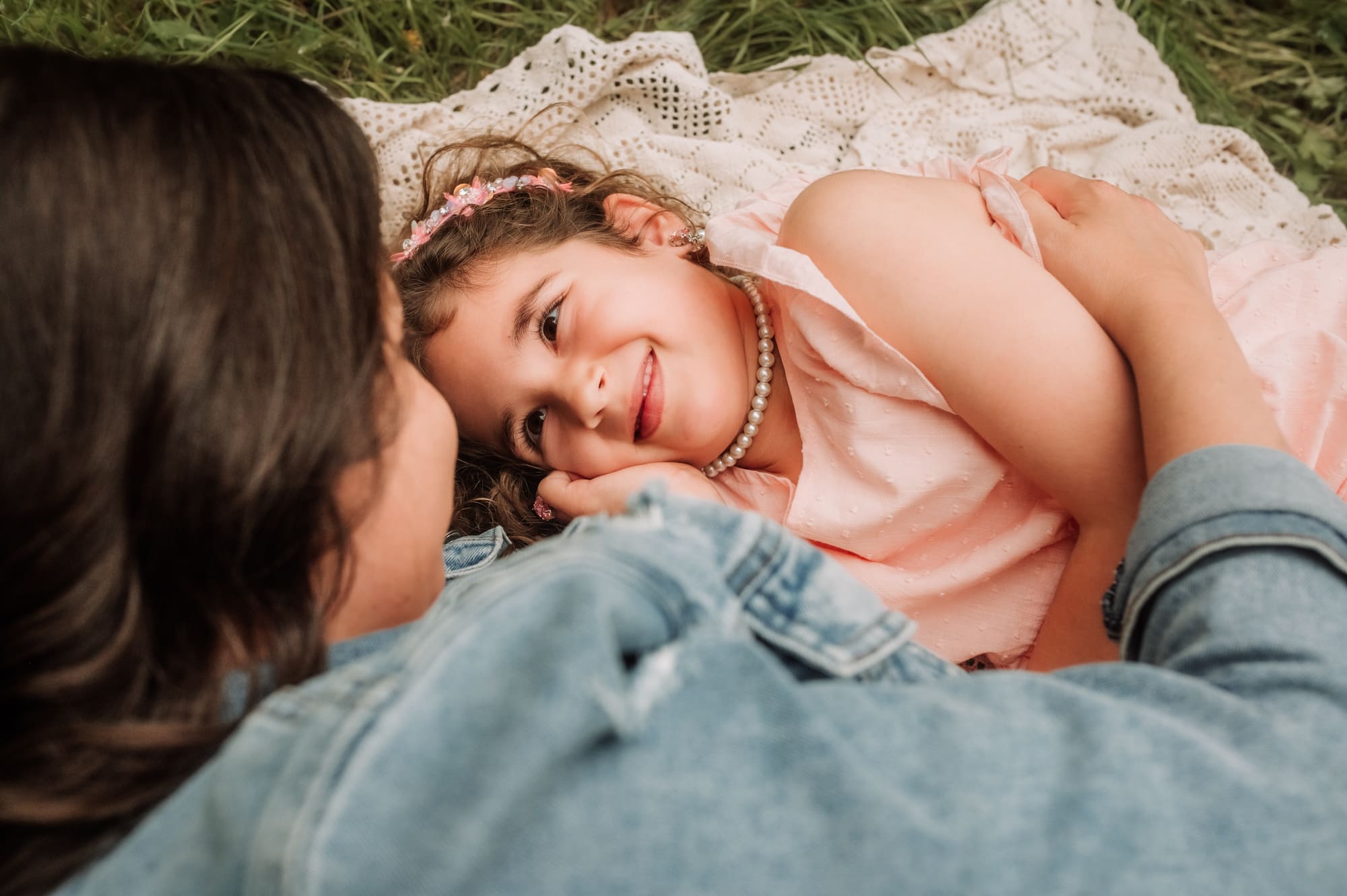 Mom and daughter lie on a blanket on the grass and share a tender look between them in this beautiful family photograph.