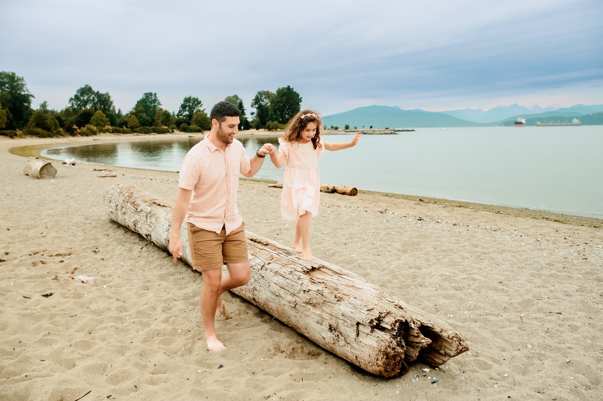 Dad leads his daughter to walk across a log at Jericho beach family photo session.